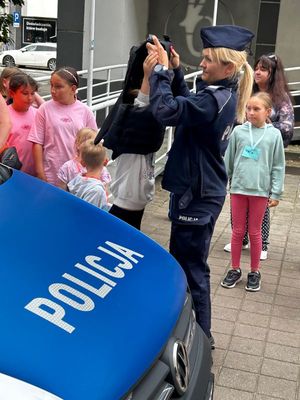 Zdjęcie przedstawiające policjantkę oraz dzieci przy radiowozie policyjnym.