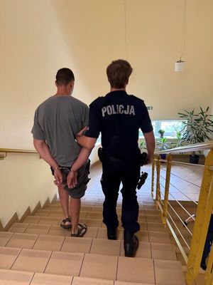 Zdjęcie przedstawiające policjanta prowadzącego zatrzymanego mężczyznę.