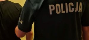 Zdjęcie poglądowe przedstawiające policjanta trzymającego pod rękę zatrzymanego mężczyznę.