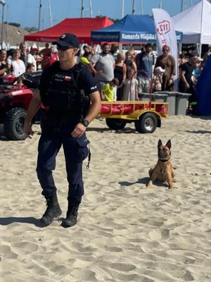 Zdjęcie przedstawiające policjanta z psem służbowym na plaży miejskiej w Gdyni.
