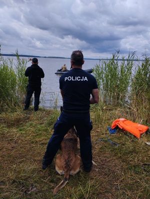 Zdjęcie przedstawiające funkcjonariuszy z psem służbowym na tle jeziora.