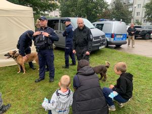 Zdjęcie przedstawiające policjantów, kobietę z dwójką dzieci, mężczyznę oraz dwa psy służbowe..