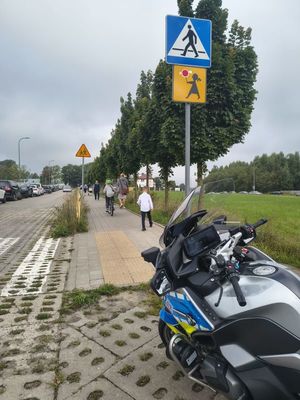 Zdjęcie przedstawiające motocykl przy przejściu dla pieszych w miejscu, gdzie dzieci idą do szkoły.