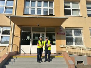 Policjantka ruchu drogowego i Strażnik miejski na tle budynku szkoły