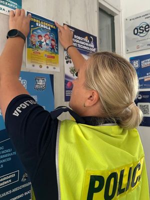 Zdjęcia przedstawia Policjantkę w szkole wieszającą plakaty
