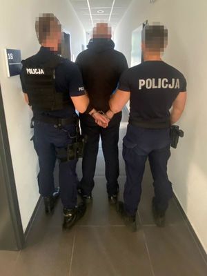 Zdjęcie przedstawiające dwóch policjantów, prowadzących zatrzymanego mężczyznę.