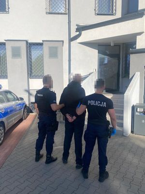 Zdjęcie przedstawiające dwóch policjantów, prowadzących zatrzymanego mężczyznę.