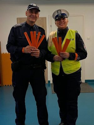 Zdjęcie przedstawiające policjantkę ruchu drogowego oraz dzielnicowego ze Śródmieścia. Funkcjonariusze trzymają w rękach opaski odblaskowe.